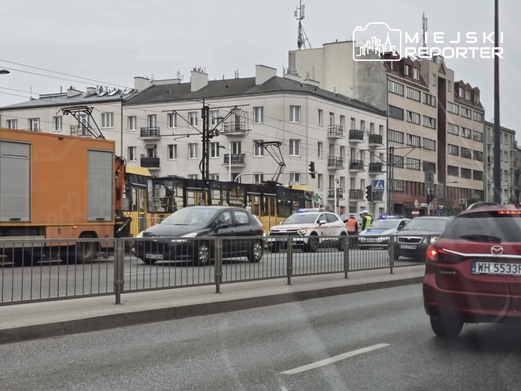 Ruch uliczny zablokowany przez policyjne samochody i pojazdy transportowe w miejskim otoczeniu.