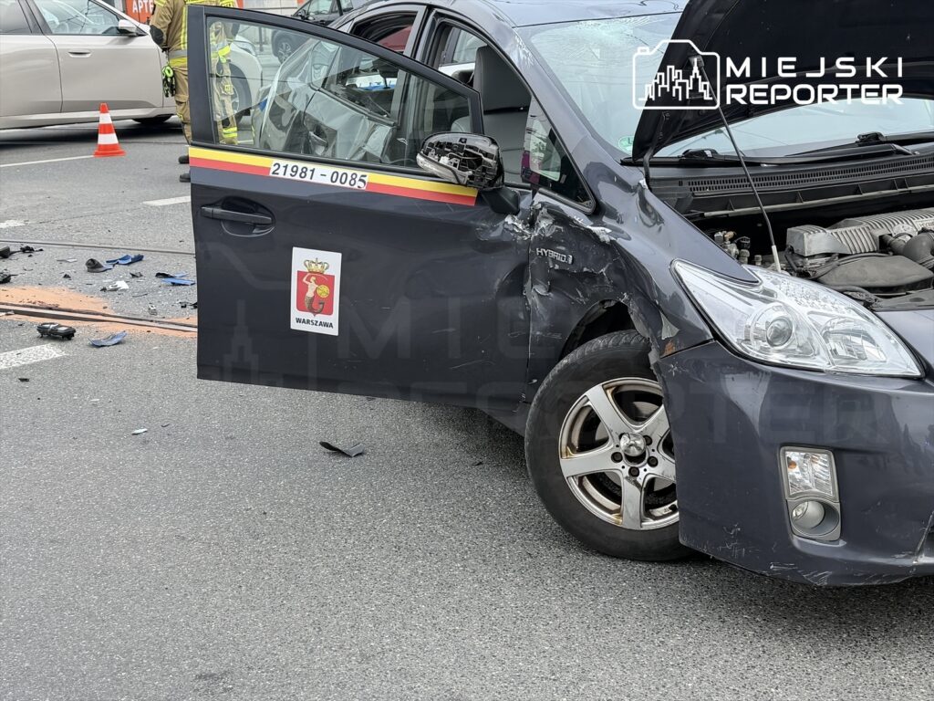 Uszkodzony samochód osobowy z otwartymi drzwiami stoi na jezdni, obok leżą fragmenty zderzenia.