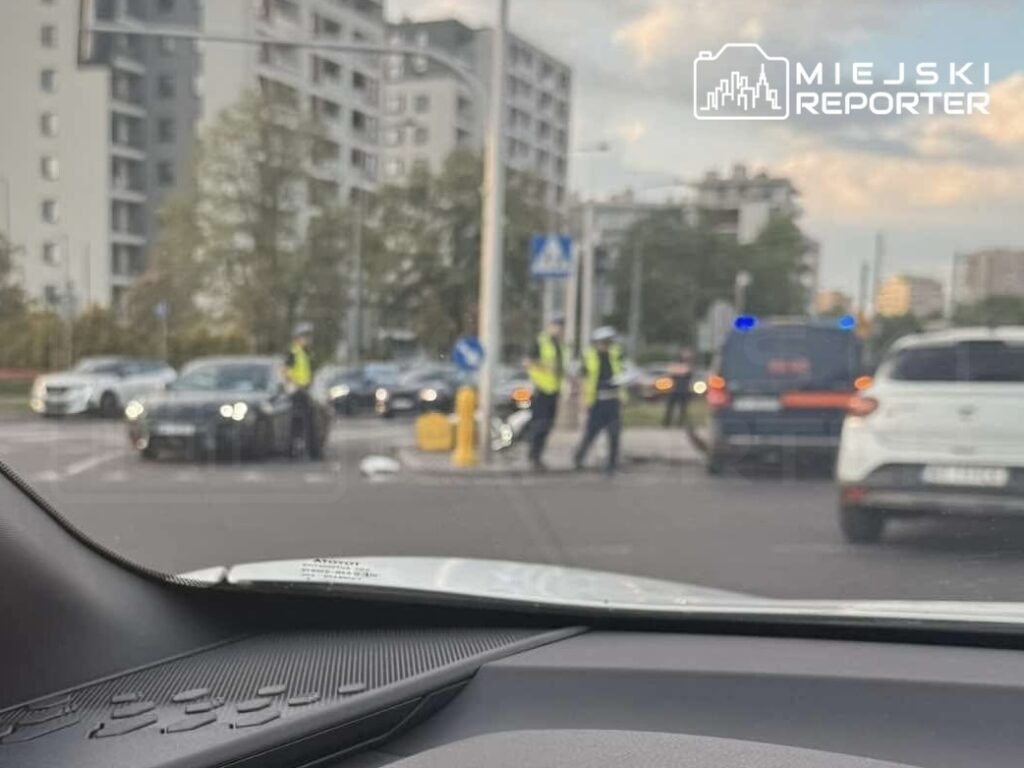 Funkcjonariusze policji przeprowadzają kontrolę drogową na skrzyżowaniu w miejskim otoczeniu.