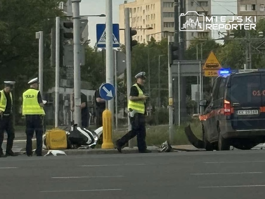 Grupa policjantów w kamizelkach odblaskowych bada miejsce wypadku drogowego obok policyjnego auta z włączonymi sygnałami.
