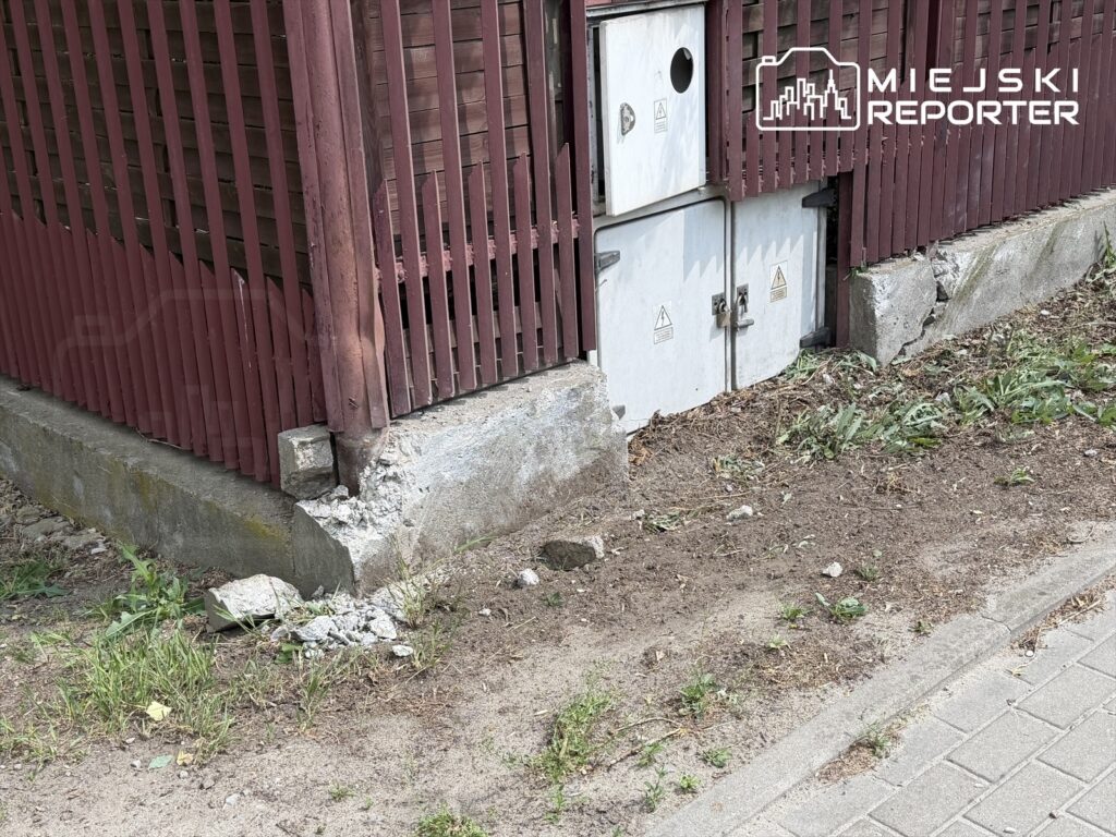 Uszkodzona podstawa drewnianego ogrodzenia z widocznymi fragmentami betonu i ziemią w otoczeniu.