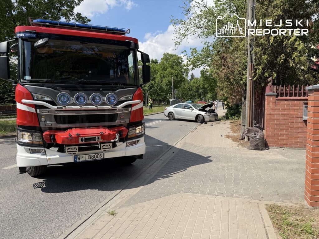 Wozidło strażackie zatrzymane na drodze obok zniszczonego samochodu osobowego leżącego na poboczu.