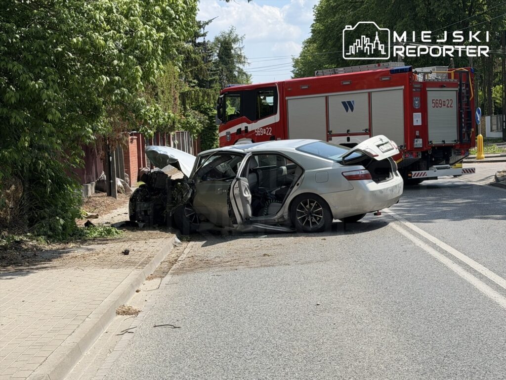 Zniszczony samochód osobowy stoi na poboczu drogi, obok widać wóz strażacki.
