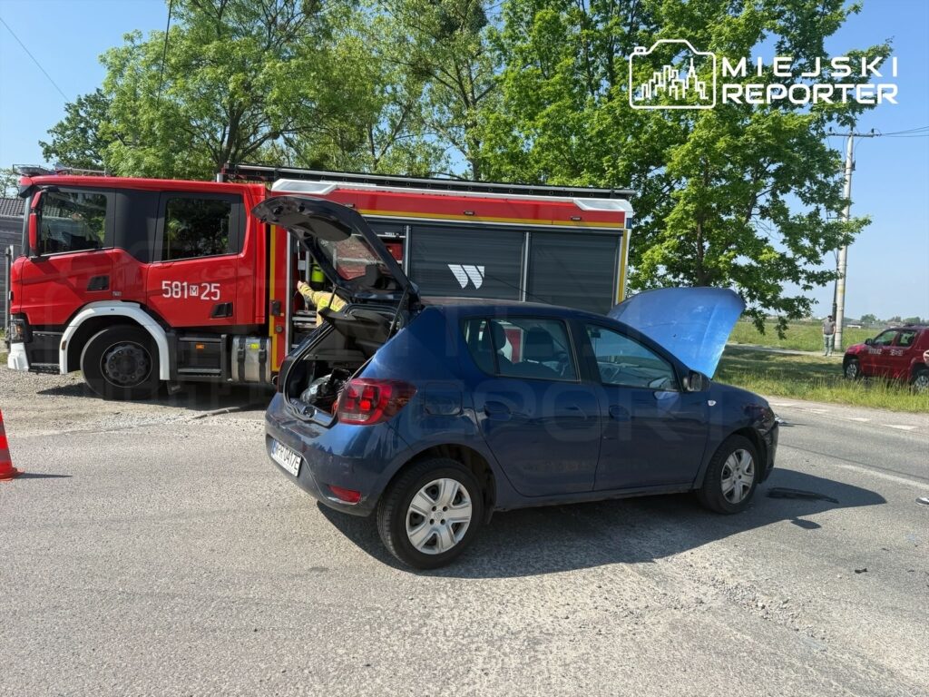 Nieoznakowany niebieski samochód osobowy z otwartą maską stoi na poboczu drogi, obok wozu strażackiego.