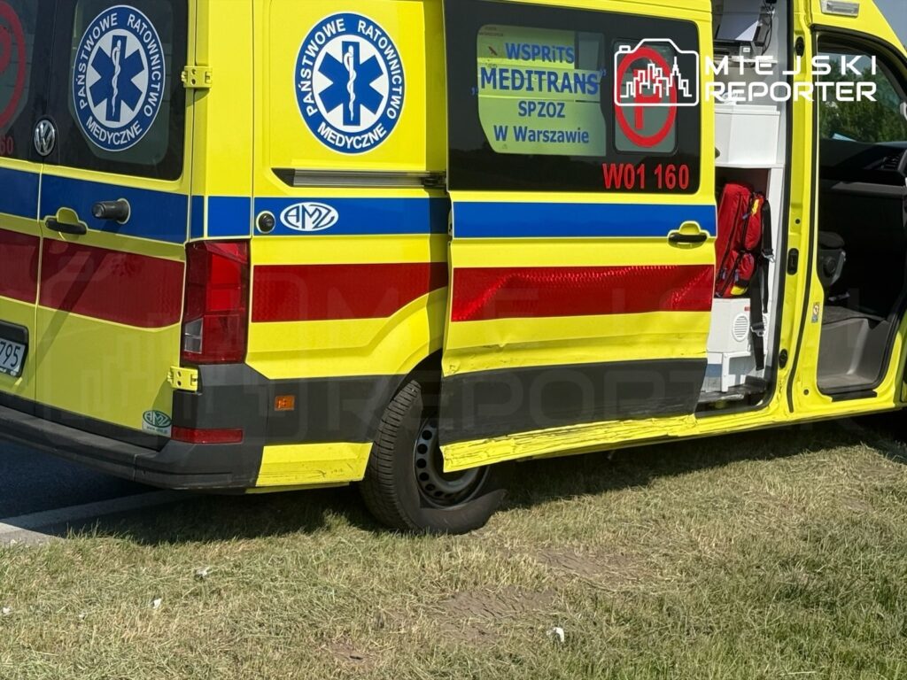 Ambulans z logo Państwowego Ratownictwa Medycznego zaparkowany na trawie, z otwartymi drzwiami tylnymi.