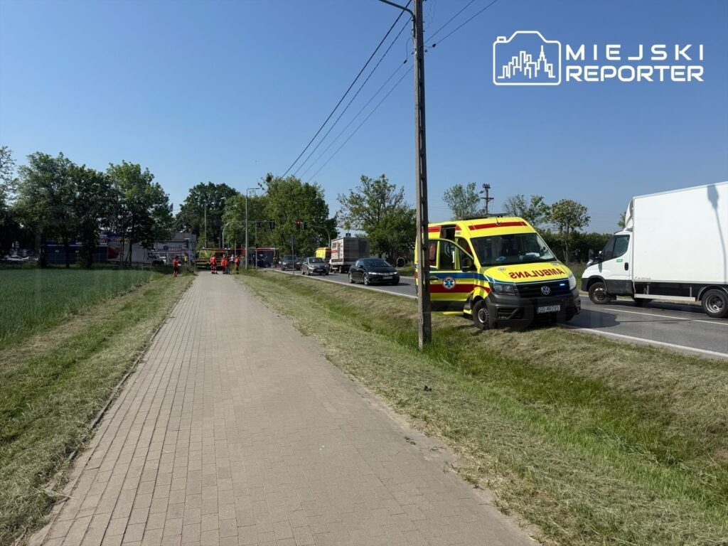 Na chodniku przy ruchliwej ulicy stoją karetki pogotowia, a obok pracują ratownicy medyczni.