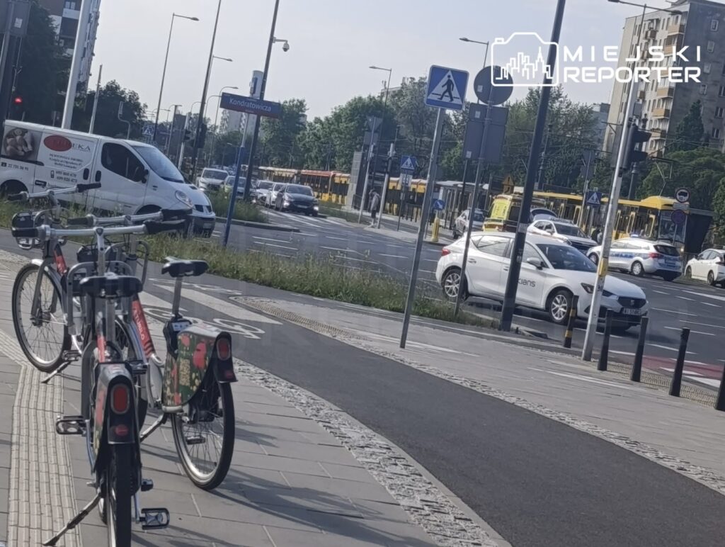 Rower miejski zaparkowany na ścieżce rowerowej obok ruchliwej ulicy z tramwajami i samochodami.