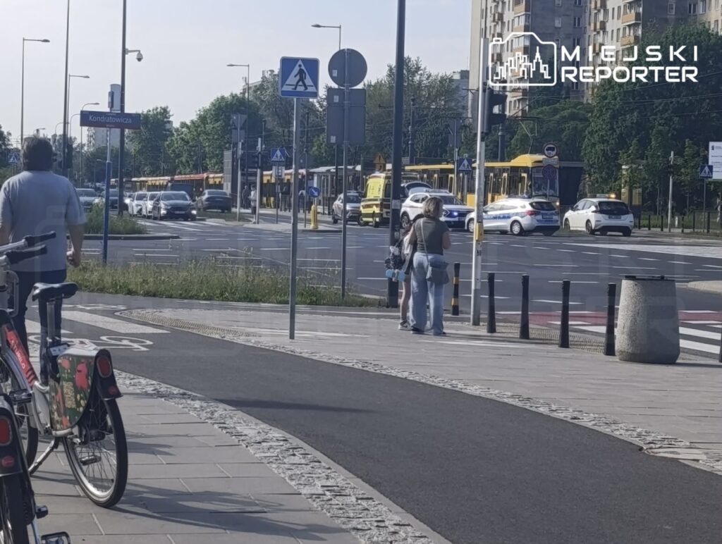 Mężczyzna spacerujący wzdłuż chodnika obok rowerów, a w tle samochody i tramwaje na ruchliwej ulicy.