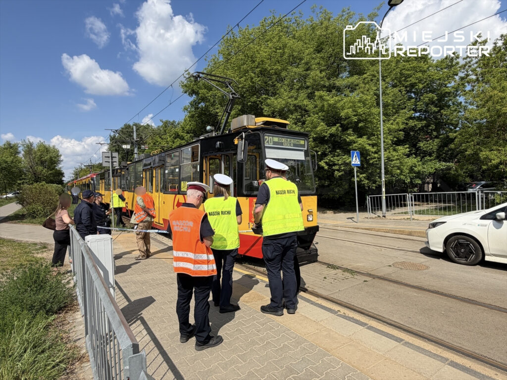 Grupa pracowników w kamizelkach odblaskowych prowadzi kontrolę przy tramwaju na przystanku w słoneczny dzień.