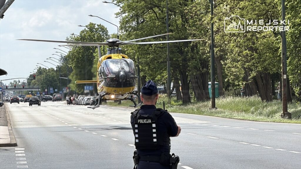 Policyjny helikopter ląduje na ruchliwej ulicy, a obok stoi funkcjonariusz w mundurze.