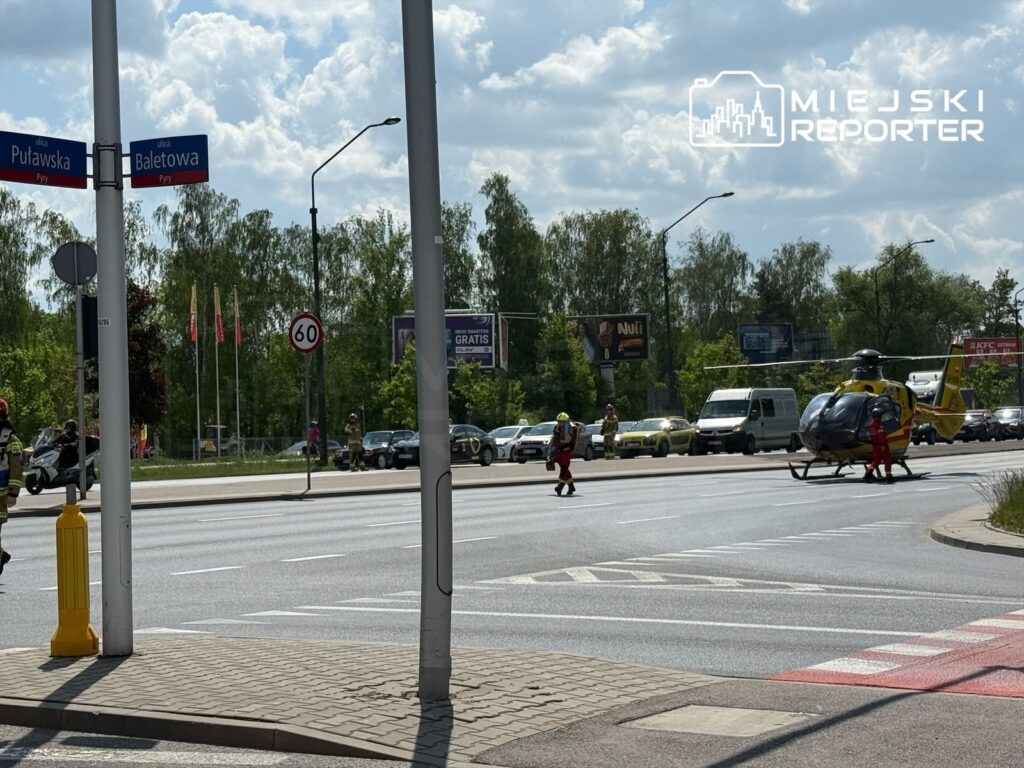 Helikopter ratunkowy ląduje na ruchliwej ulicy, obok grupy ratowników i samochodów stojących w korku.