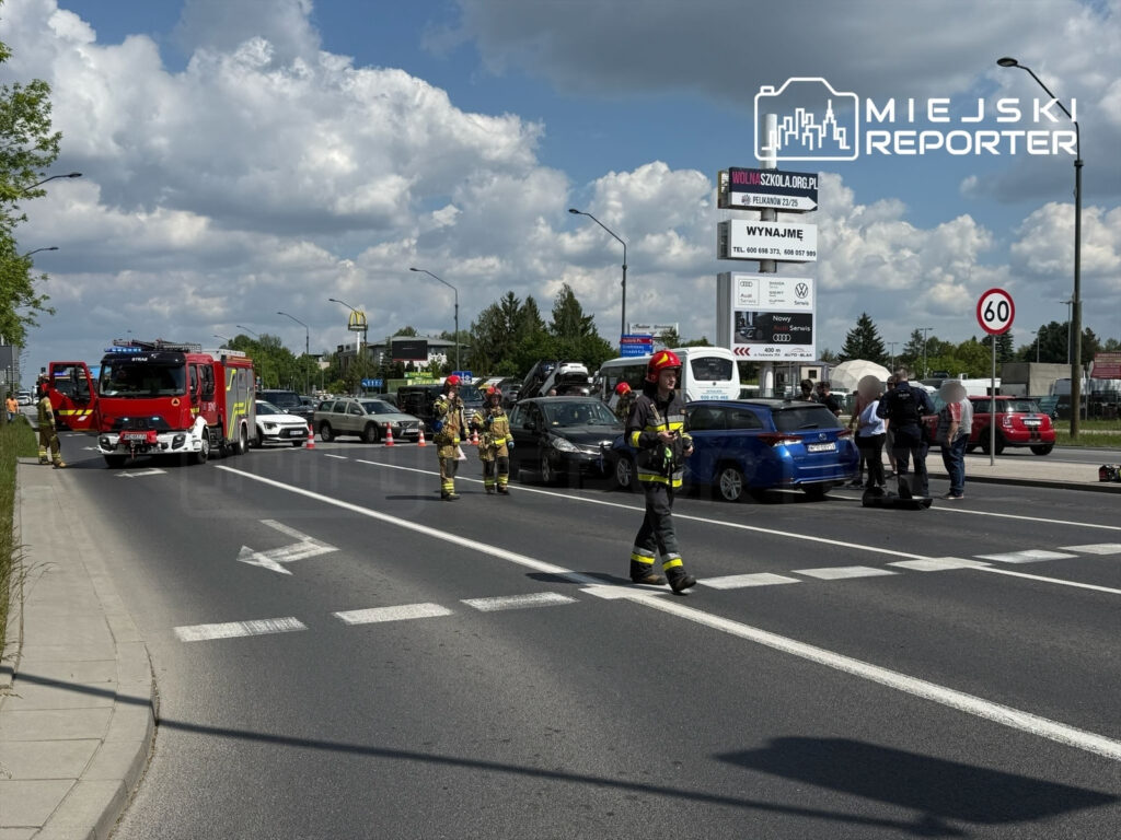 Na drodze stoi wóz strażacki, a strażacy udzielają pomocy przy zderzeniu dwóch samochodów osobowych.