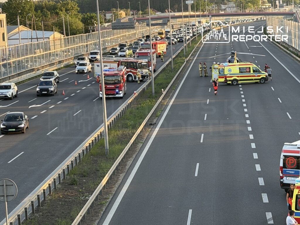 Na drodze ekspresowej zatrzymane pojazdy i służby ratunkowe, w tym ambulans i wóz strażacki, prowadzą działania.