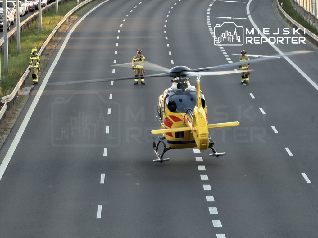 Śmigłowiec ratunkowy lądował na autostradzie, a obok stoją strażacy w uniformach.