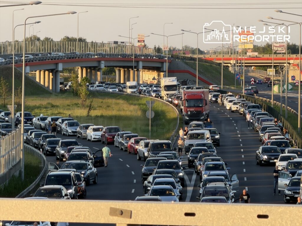 Ruch samochodowy na zakorkowanej drodze, z kierowcami wychodzącymi z pojazdów w ciepłe popołudnie.