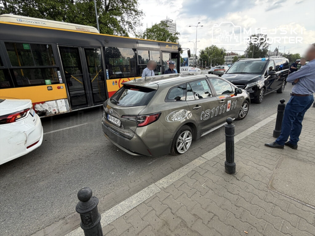 Zatrzymany autobus komunikacji miejskiej obok taksówki, w otoczeniu innych pojazdów na ruchliwej ulicy.