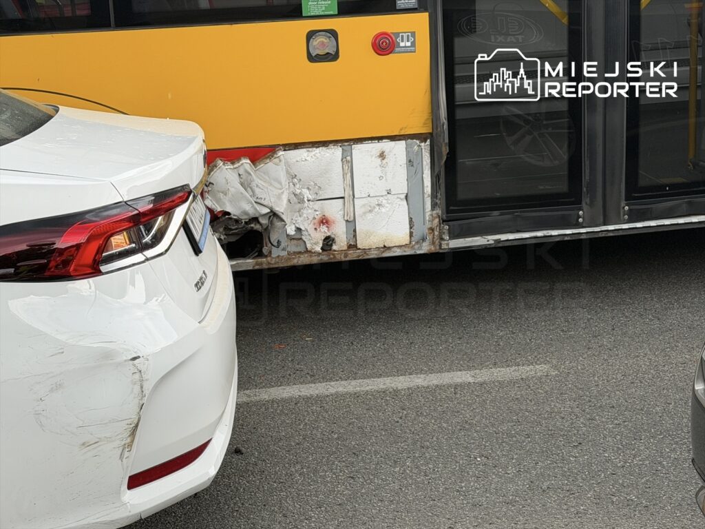 Biały samochód osobowy z uszkodzeniem tylnego zderzaka zderza się z żółtym autobusem na ruchliwej ulicy.