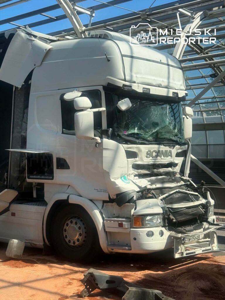 Uszkodzony biały ciągnik siodłowy marki Scania z wybitym przednim szkłem stoi na terenie budowy, z uszkodzoną kabiną.