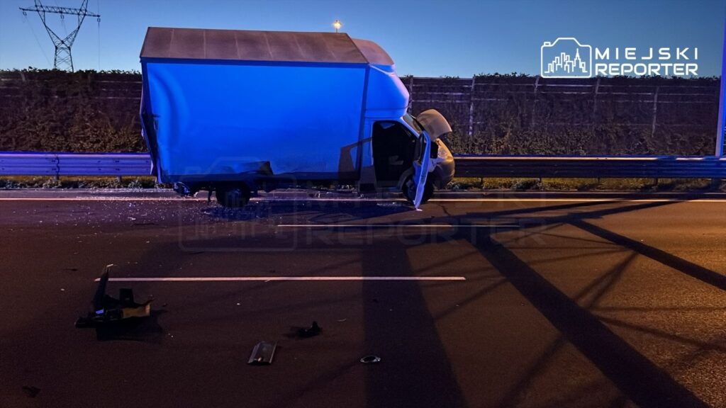 Zniszczony samochód dostawczy na autostradzie, z otwartymi drzwiami i odłamkami na jezdni.