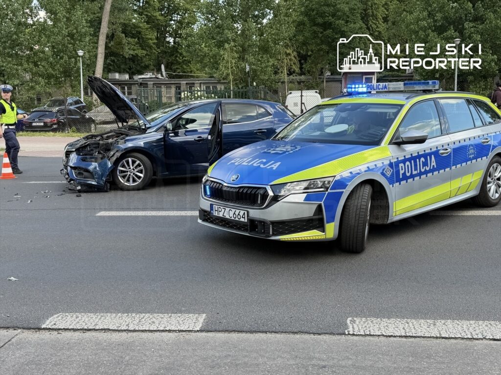Policyjny radiowóz z włączonymi sygnałami świetlnymi stoi obok uszkodzonego samochodu osobowego na drodze.