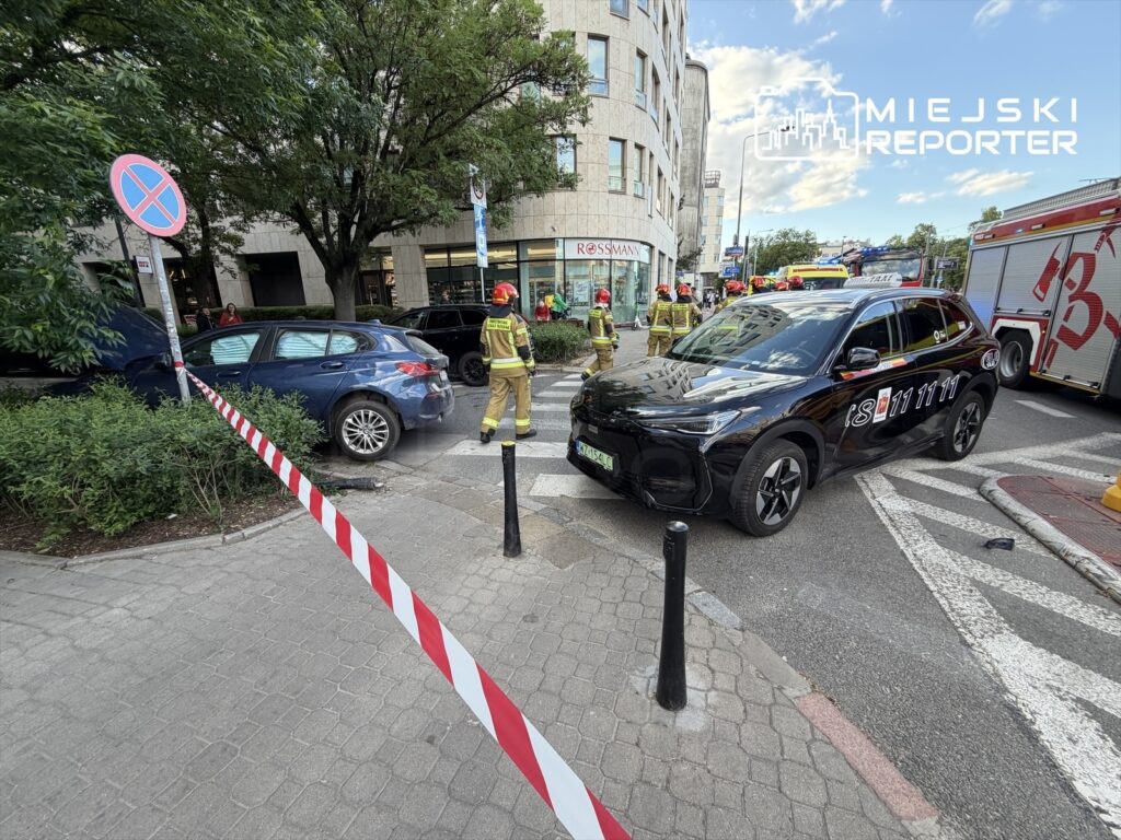 Strażacy pracują przy wypadku drogowym, otaczając uszkodzone pojazdy taśmą zabezpieczającą na ruchliwej ulicy.