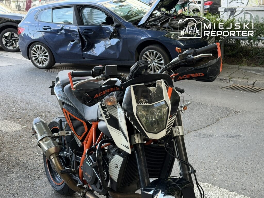Motocykl sportowy stoi na ulicy obok uszkodzonego samochodu osobowego z wgniecioną boczną częścią.