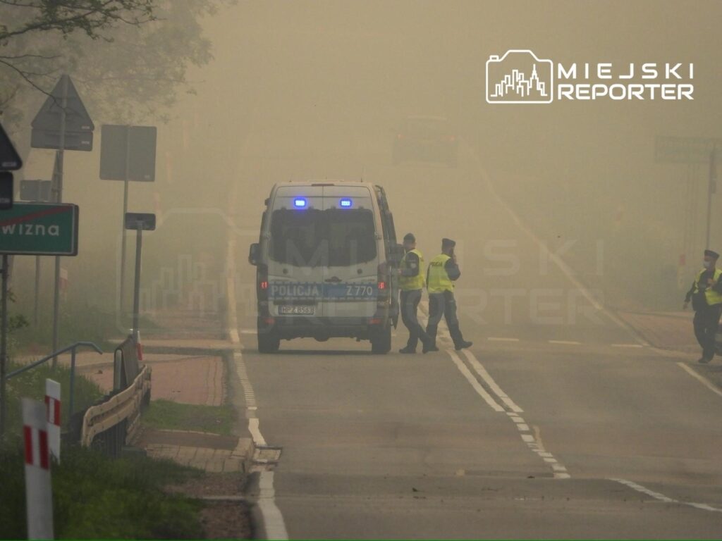Policjanci kontrolują ruch drogowy w gęstej mgle, obok radiowozu na zablokowanej drodze.