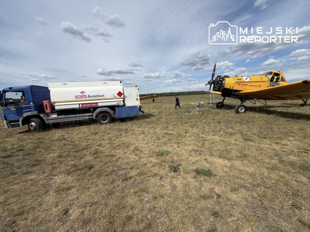Samolot rolniczy w kolorze żółtym stoi na trawie, obok niego ciężarówka z paliwem Orlen Aviation.