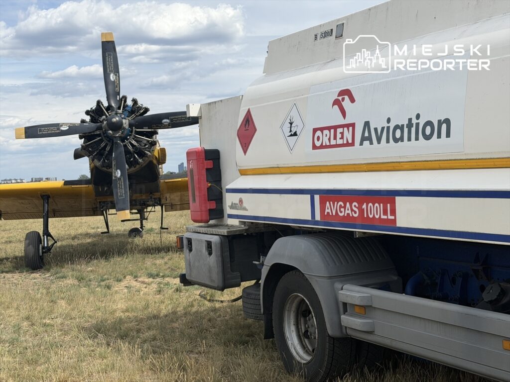 Samolot rolniczy z widocznym silnikiem i śmigłem stoi na polu obok cysterny z paliwem ORLEN Aviation.