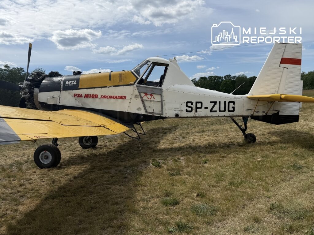 Samolot rolniczy PZL M18B Dromader stoi na trawie w słonecznym otoczeniu, z widocznym silnikiem i żółtymi skrzydłami.