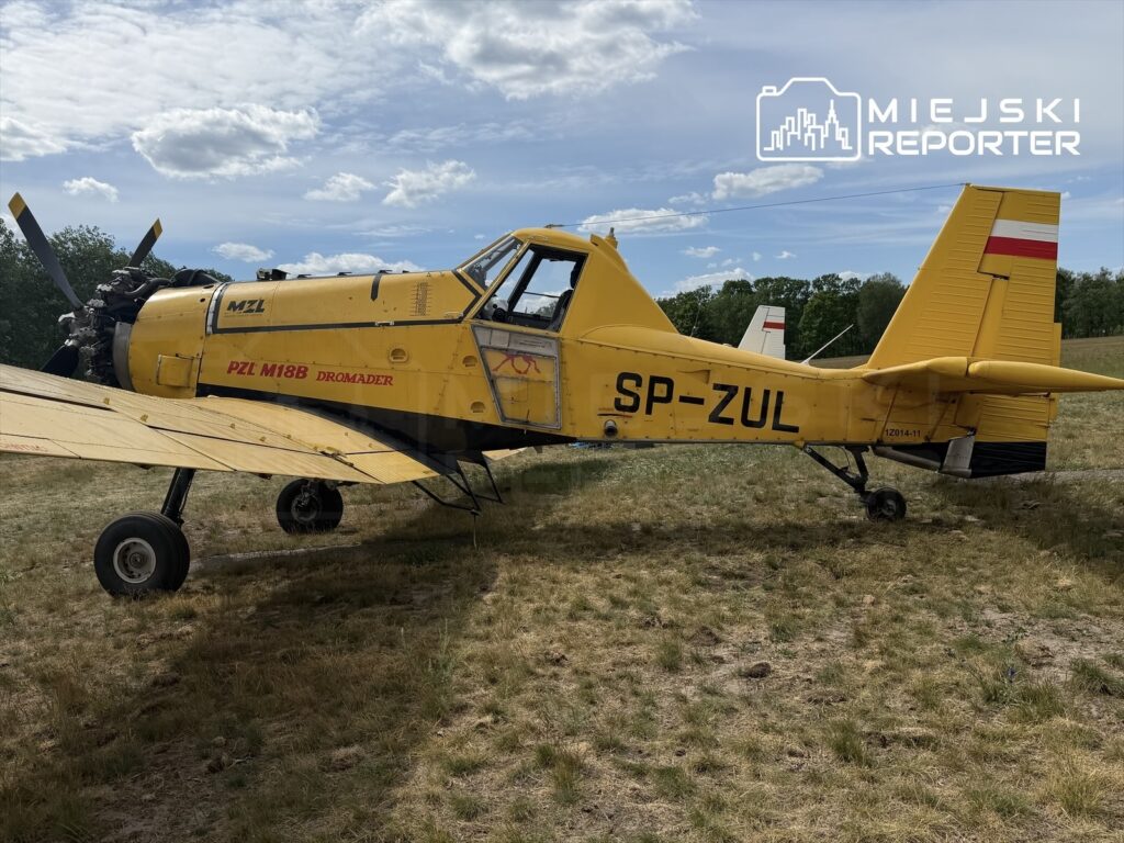Żółty samolot rolniczy PZL M18B Dromader stoi na trawiastej nawierzchni w słonecznym otoczeniu.