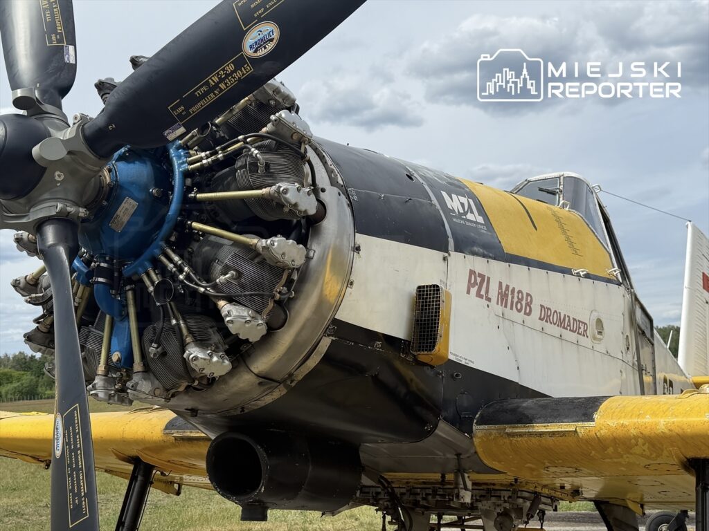 Silnik samolotu PZL M18B Dromader z widoczną śmigłem i detalami konstrukcyjnymi, stojącego na trawie w otoczeniu chmur.