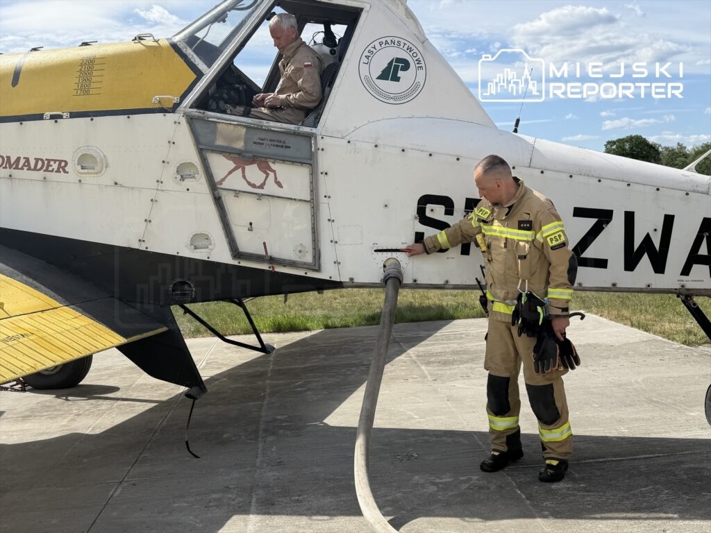 Pilot w kabinie samolotu gaśniczego przygotowuje się do lotu, podczas gdy strażak podłącza wąż do zbiornika.