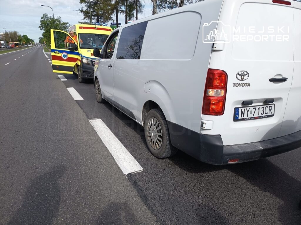 Karetka pogotowia z otwartymi drzwiami zatrzymana obok białego furgonu na drodze.