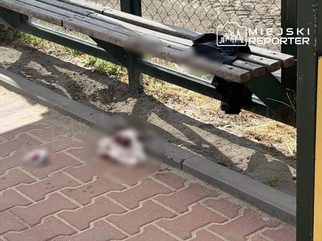 Na chodniku przy przystanku autobusowym leżą plamy krwi, obok znajduje się opuszczona odzież.