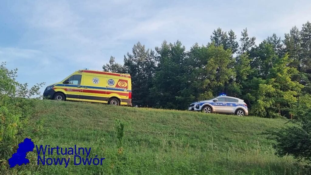 Karetka pogotowia i radiowóz policyjny zatrzymane na wzgórzu w otoczeniu drzew, w tle błękitne niebo.