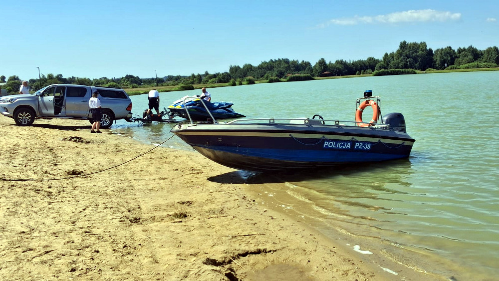 Policjanci przygotowują łódź motorową do wodowania na piaszczystym brzegu w słoneczny dzień.