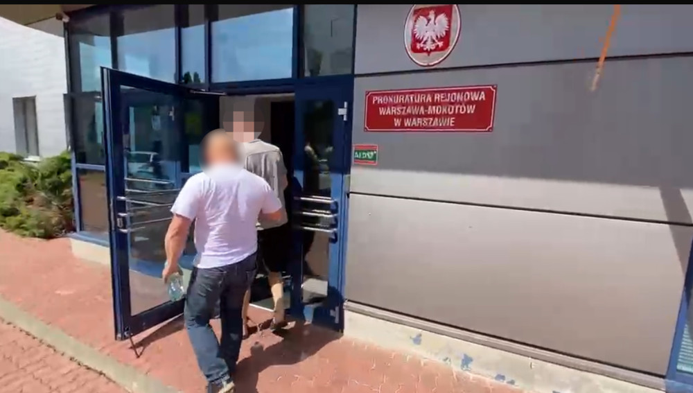Dwaj mężczyźni wchodzą do budynku prokuratury z widocznym znakiem "Prokuratura Rejonowa Warszawa-Mokotów".