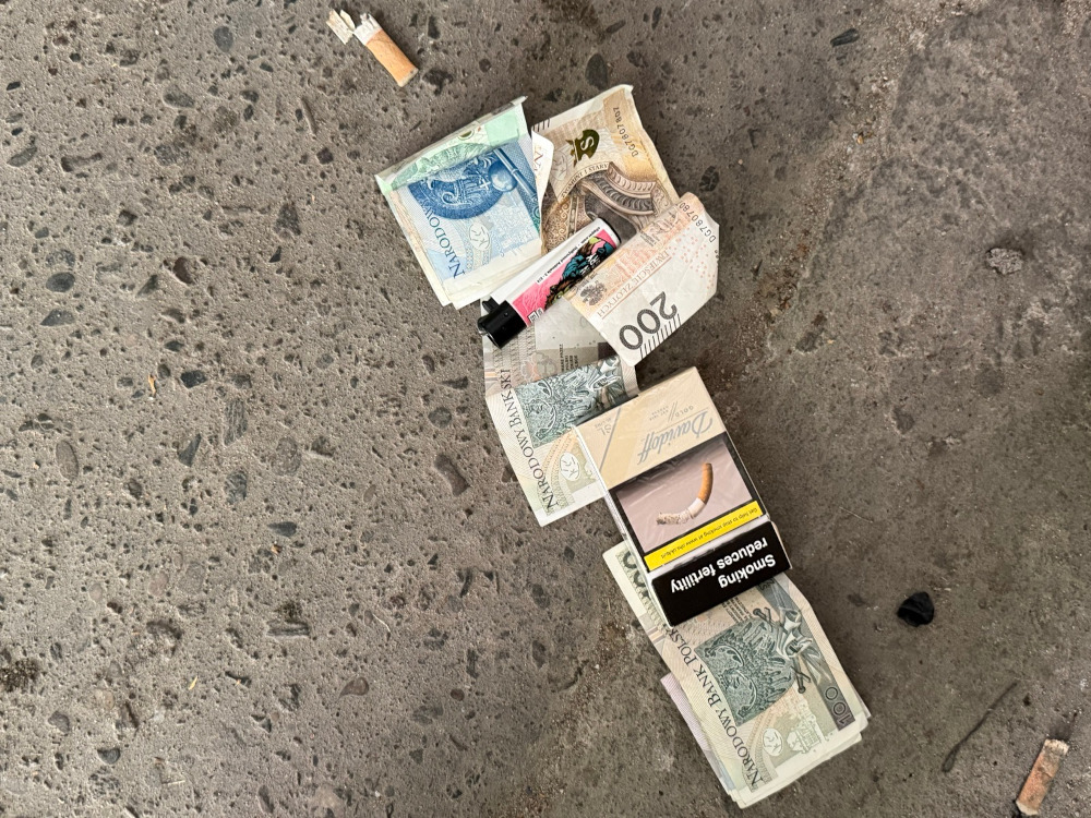 Na szarej powierzchni leżą banknoty, paczka papierosów oraz zapalniczka.