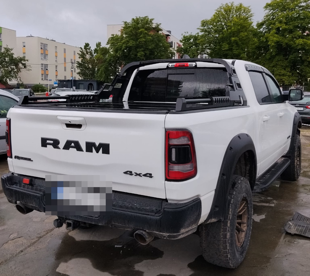 Biały pickup RAM 4x4 zaparkowany na parkingu, w tle widoczne budynki mieszkalne i zieleń drzew.