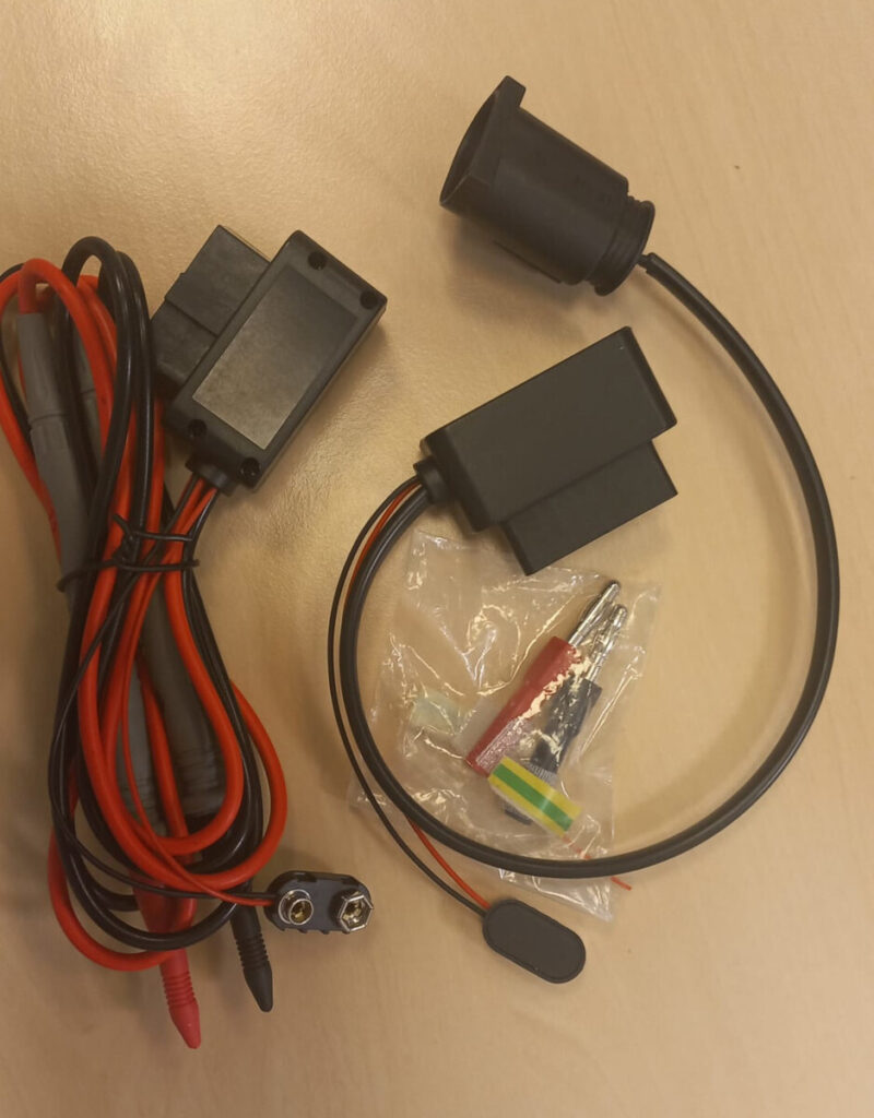 Zestaw przewodów i złączy elektrycznych na drewnianym biurku, w tym czujnik i elementy montażowe.