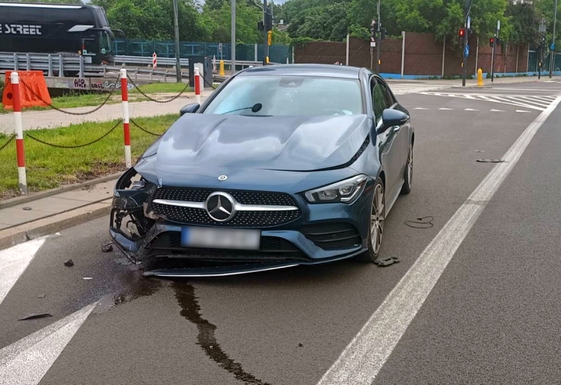 Uszkodzony samochód osobowy marki Mercedes z wgniecionym przodem stoi na skrzyżowaniu ulicy.