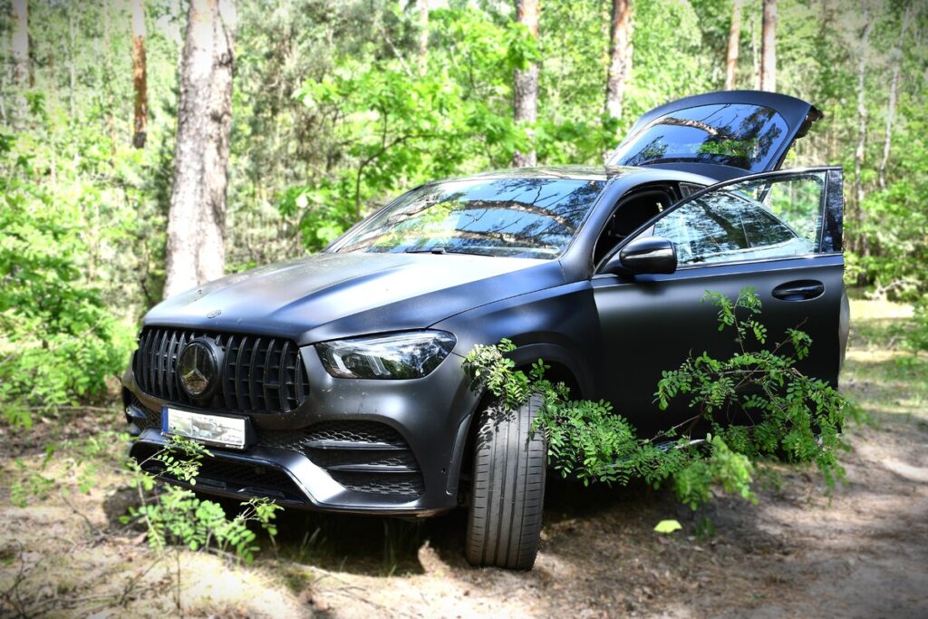 Nowoczesny SUV w matowej czerni stoi na leśnej drodze, z otwartymi drzwiami i widoczną roślinnością wokół.