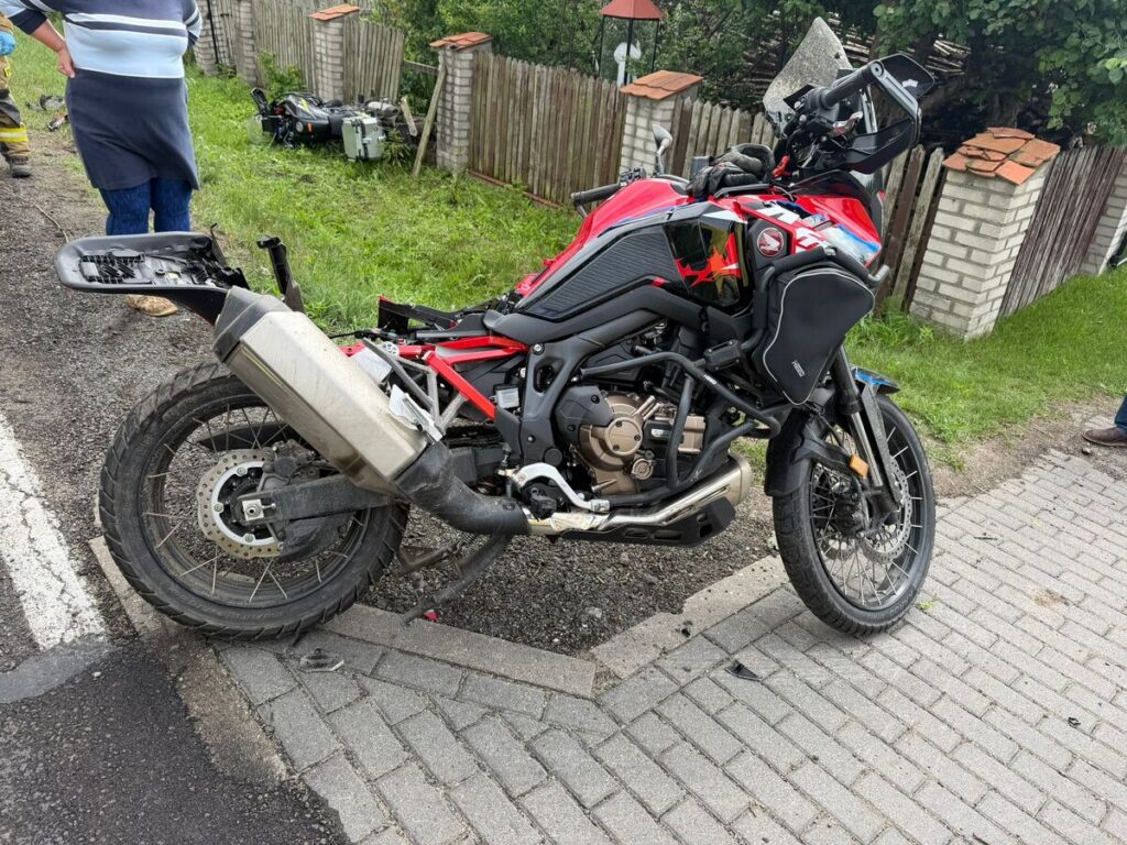 Uszkodzony motocykl leży na boku przy drodze, obok stojący mężczyzna w niebieskiej koszuli obserwuje sytuację.