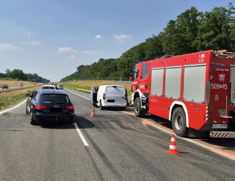 Na drodze ekspresowej stoi czarne audi i białe auto dostawcze z otwartymi drzwiami, obok czerwony wóz strażacki.