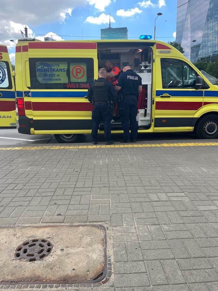 Ratownicy medyczni i policjanci współpracują przy ambulansie w miejskim otoczeniu.