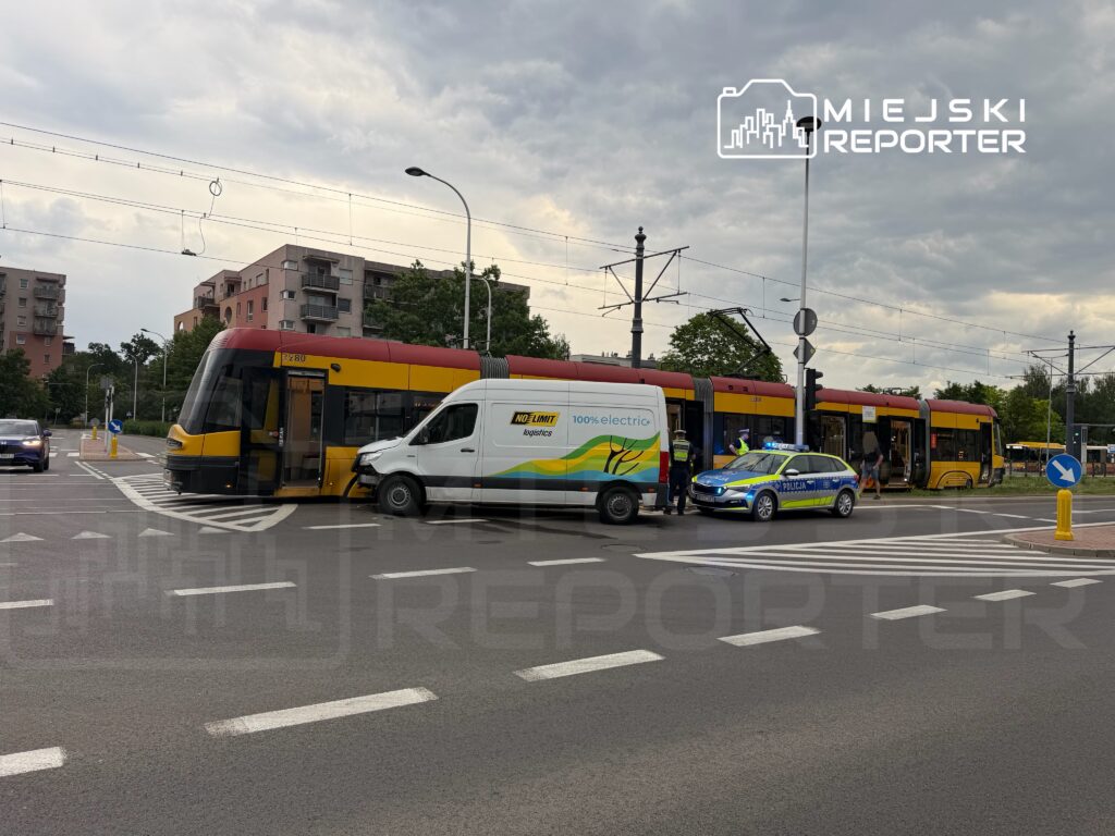 Tramwaj zatrzymany na skrzyżowaniu, obok uszkodzony furgon dostawczy oraz radiowóz policyjny. W tle blokowiska.