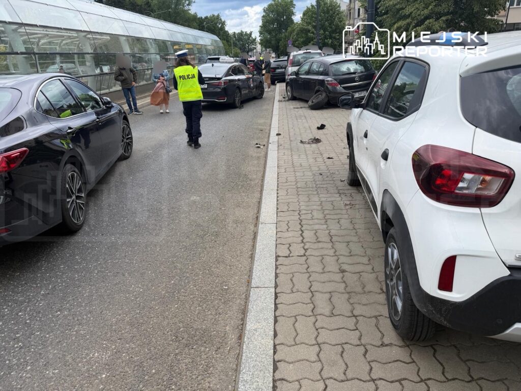 Policjant w kamizelce odblaskowej kieruje ruchem obok zderzonych samochodów na miejskiej ulicy.
