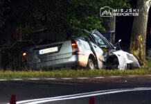 Samochód osobowy w kolorze szarym, uszkodzony i częściowo wjeżdżający w zieleń, obok drogi, w nocy.