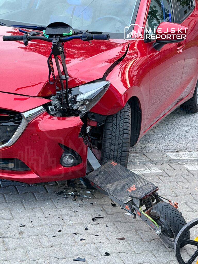Czerwony samochód osobowy z uszkodzoną przednią częścią, obok stoi uszkodzony skuter elektryczny.